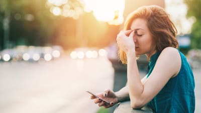 stressed woman leaning on railing looking at her phone